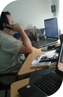 Hombre en un escritorio con dos laptops y un teléfono, concentrado en su trabajo y gestionando tareas simultáneamente.