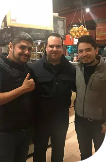Tres hombres sonrientes posan juntos en un restaurante, transmitiendo camaradería y buena compañía.
