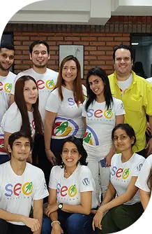 Grupo de personas sonriendo, vestidas con camisetas del logo de SEO, en un ambiente de trabajo colaborativo.